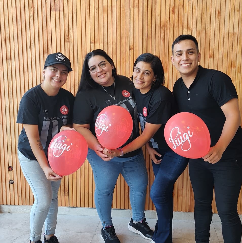Cuatro integrantes del equipo de Luigi sonriendo con globos rojos de la marca.